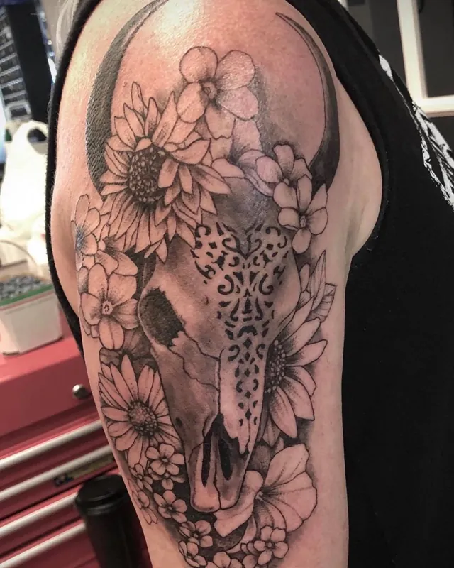 Animal skull surrounded by sunflowers and blossoms on an upper arm.