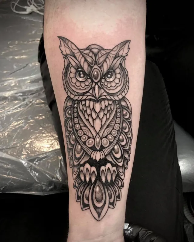 An owl forearm tattoo with layered ornamental feather patterns.