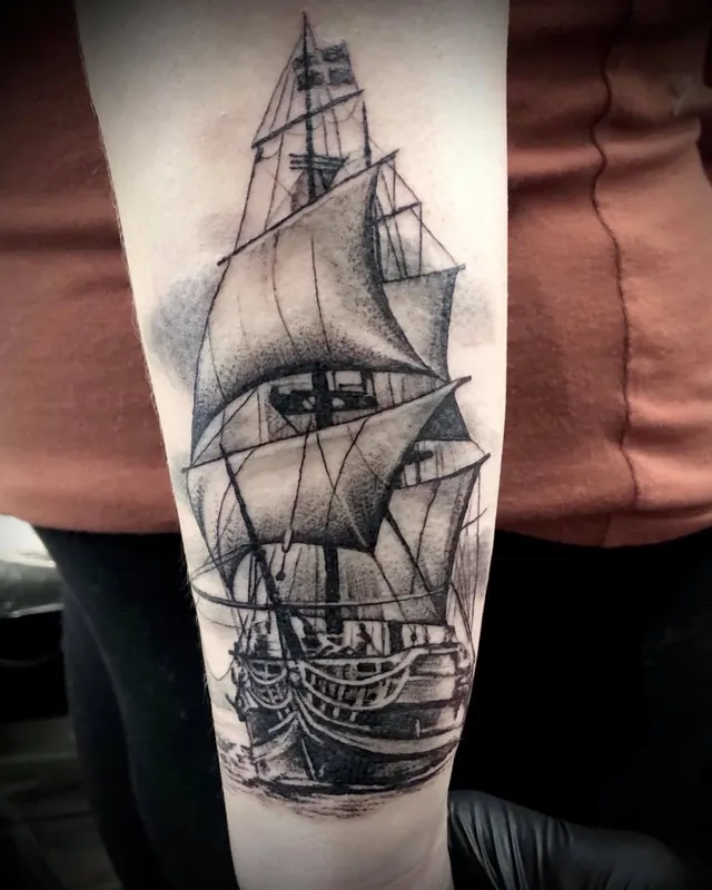 A black and grey sailing ship tattoo on a forearm.