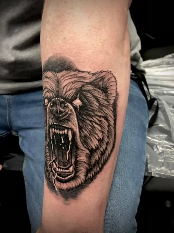 Side view of a roaring bear head tattoo on a forearm.