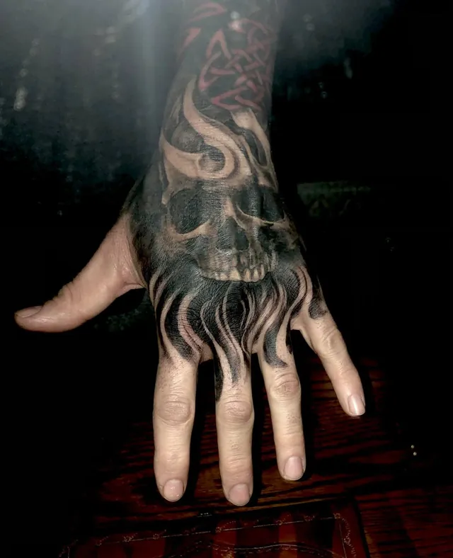 A skull with flowing flames tattooed across the hand and wrist.