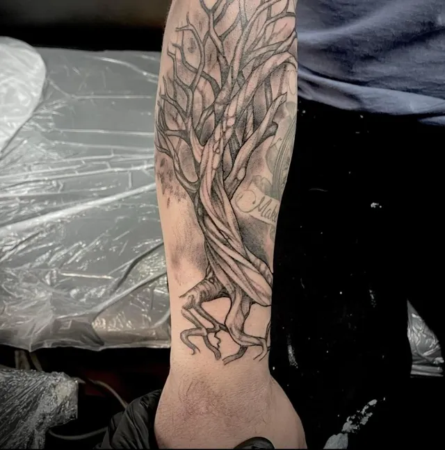 A branching tree with exposed roots tattooed along a forearm.