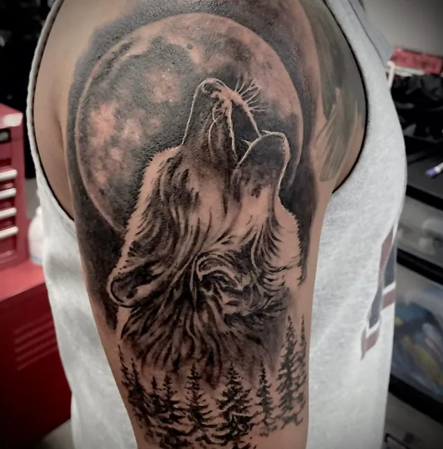 A howling wolf beneath a large moon tattooed on an upper arm.