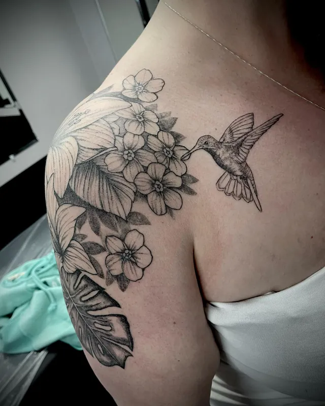 A hummingbird beside tropical flowers across a shoulder.
