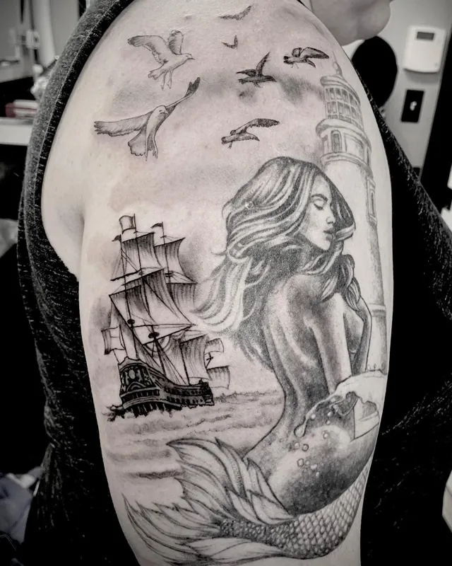 A mermaid, sailing ship, lighthouse and seabirds in an upper-arm tattoo.