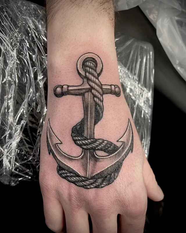 An anchor wrapped in rope tattooed across the wrist and back of the hand.